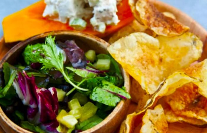 a traditional homemade Hawaiian meal featuring salad, chips, and papaya