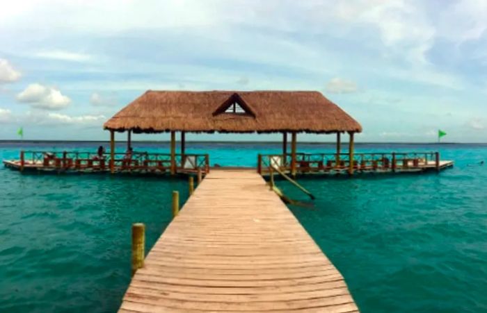 A wooden deck extends over the vibrant Seven Colors Lagoon in Costa Maya.