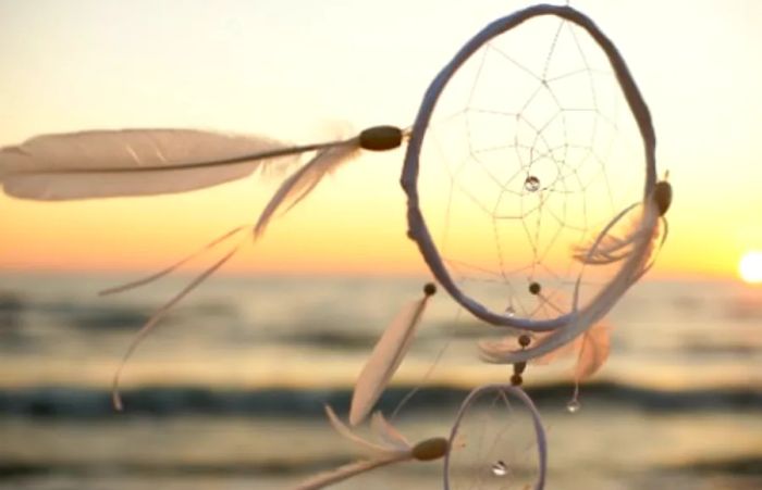 a white dream catcher swaying in the ocean breeze during sunset