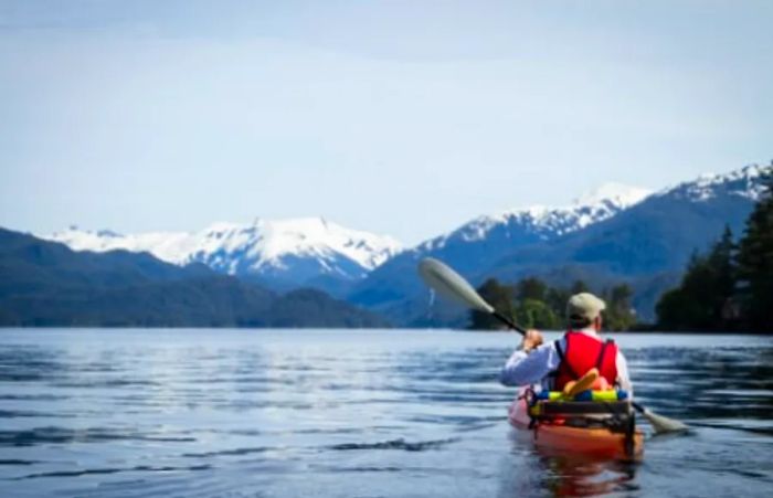 a kayaker paddling near the shores of Sitka, Alaska, with snow-capped mountains in the distance