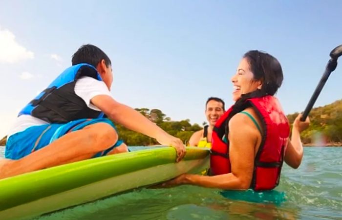 A family assisting their child onto a paddle board at a Caribbean beach