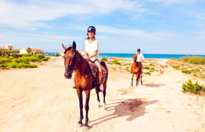 a woman riding a horse along the beach in Half Moon Cay with her husband following behind