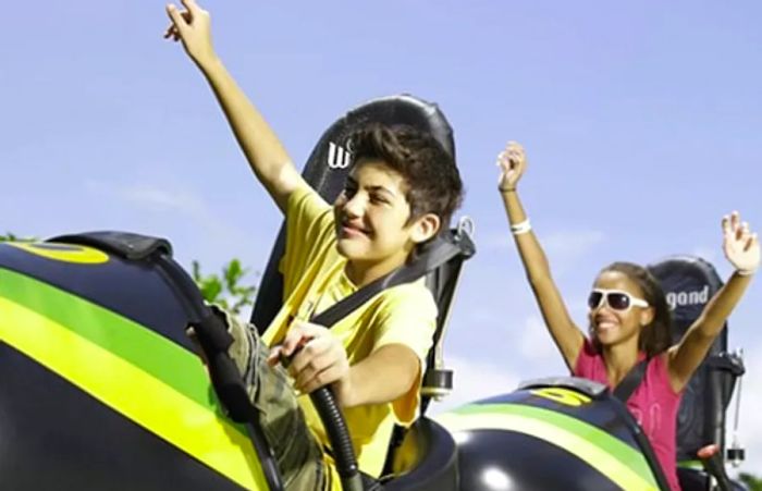 A young boy and girl joyfully raising their hands as they zoom down a bobsled in Montego Bay.