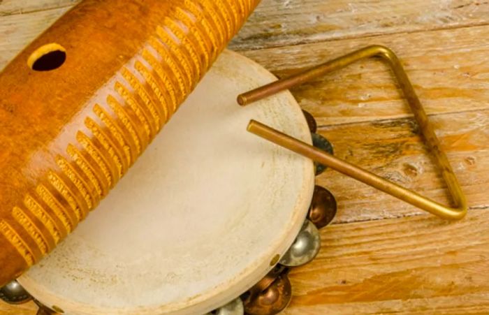 A wooden güiro, tambourine, and musical triangle arranged on a table