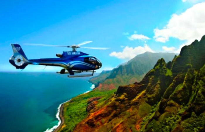 A blue helicopter gliding over Hawaii's lush green mountains