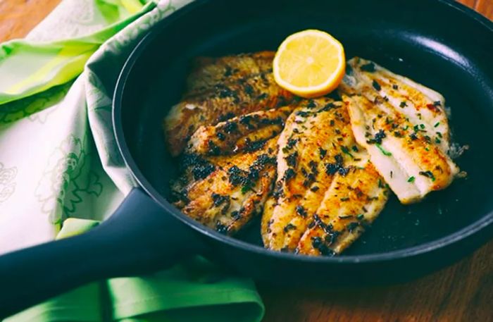 Four fish fillets cooked in a pan with fresh lemon slices