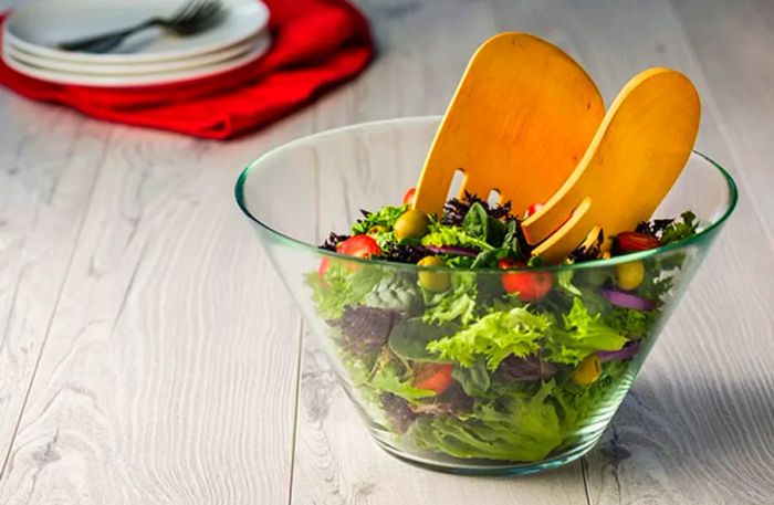 two wooden bear claw servers placed in a bowl of salad