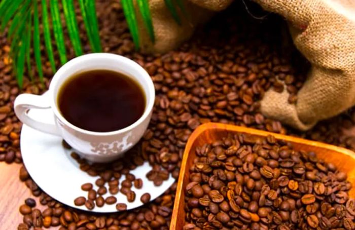 coffee beans scattered on a table beside a small cup of brewed coffee