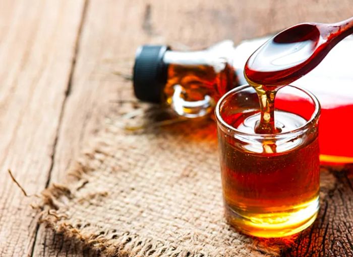 birch syrup being poured into a glass with a syrup bottle in the background