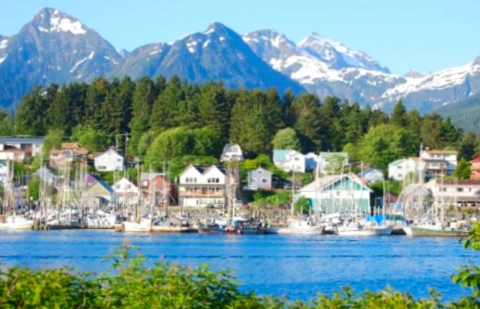 A picturesque view of Sitka Harbor from across the water, framed by snow-capped mountains in the background