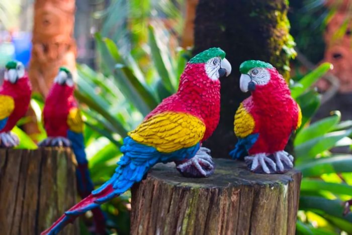 vibrant red, yellow, and blue parrot sculptures perched on wooden logs