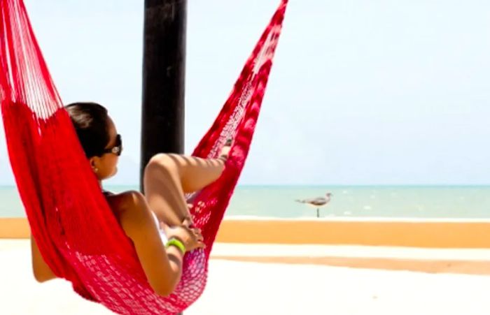 a woman lounging on a red hammock with a view of the beach in Progreso