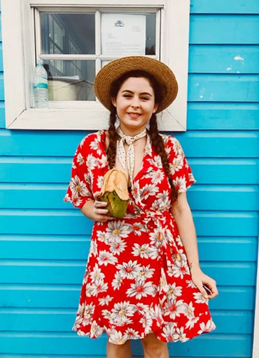 Noelle sipping from a coconut in front of a bright blue building