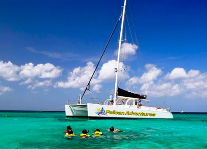 individuals snorkeling among the coral reefs in Aruba while others relax on a catamaran