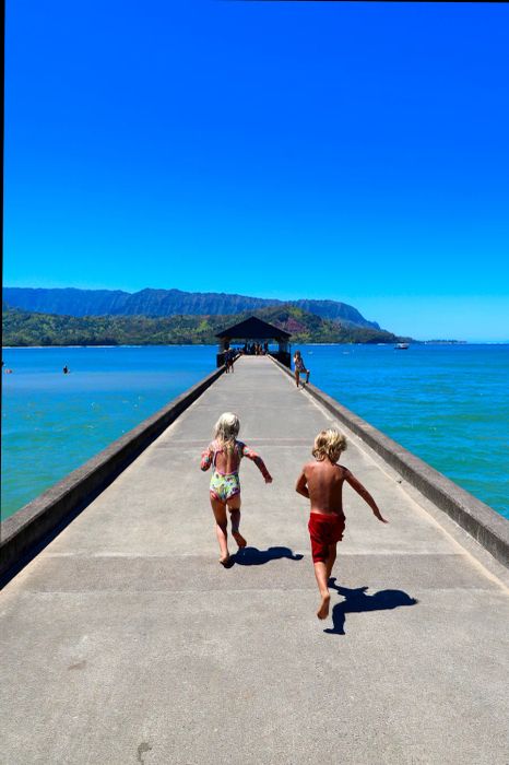 children sprinting on a pier surrounded by water