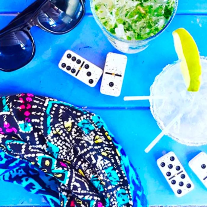 Aerial view of beverages, dominos, and sunglasses laid out on a blue table