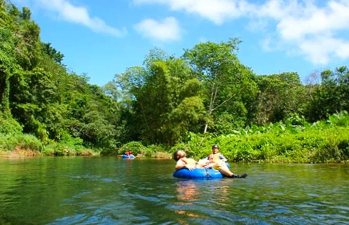 Two men relish their river tubing adventure along the serene waters in Dominica