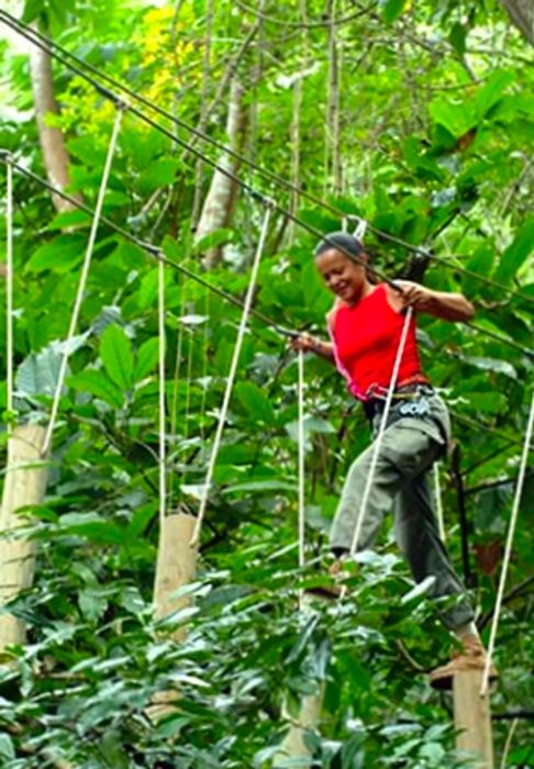 A woman carefully navigates a suspended platform bridge during a canopy challenge