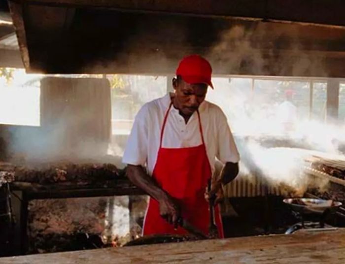 A man in a red hat and apron grilling jerk chicken in Montego Bay