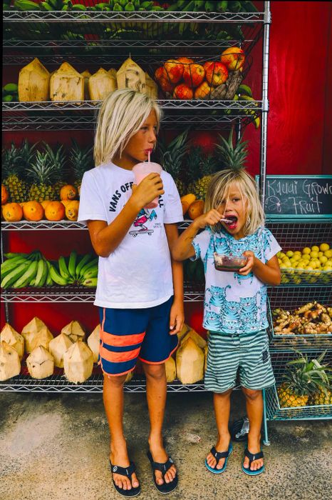 children enjoying snacks in front of a fruit stand