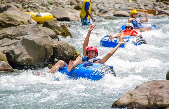 A man raises his hands in excitement while river tubing down the Layou River, with other guests trailing behind him