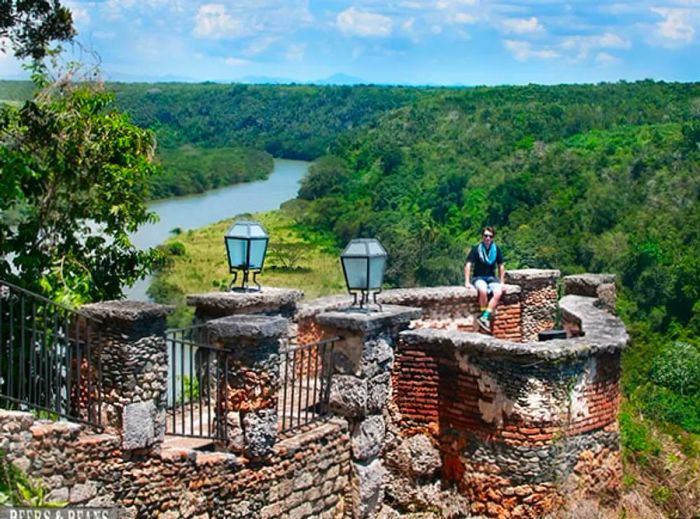 Randy perched on a wall in La Romana, with trees and the Chavón River visible in the background