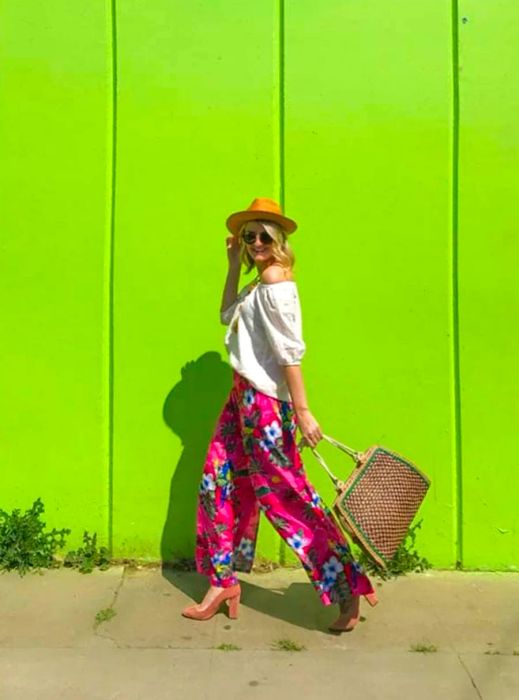 A woman posing confidently with her bag in front of a vibrant green wall