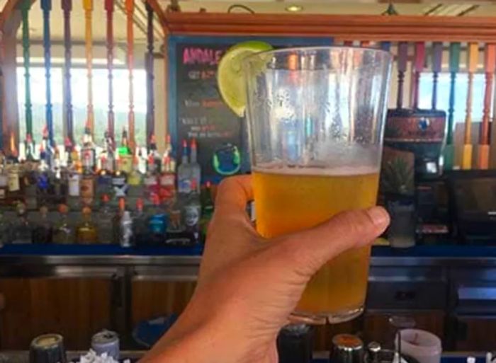 A hand holding a glass of beer with the bar in the background