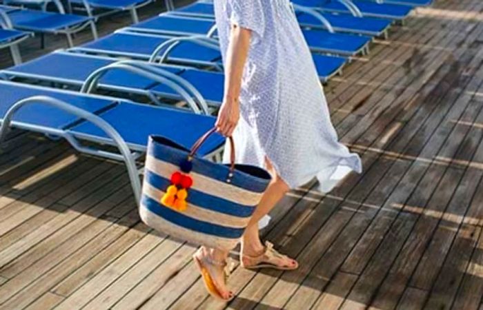 Caroline carrying a blue and tan striped bag adorned with colorful tassels by the pool