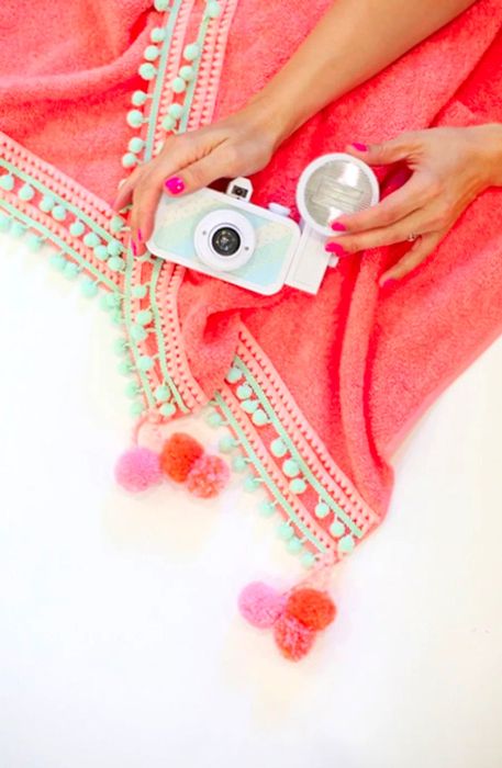 Hands with a camera resting on the DIY pompom beach towel