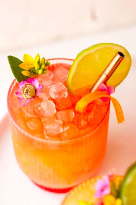 Pineapple mango rum punch cocktail adorned with edible flowers, a lime slice, and a hint of orange zest