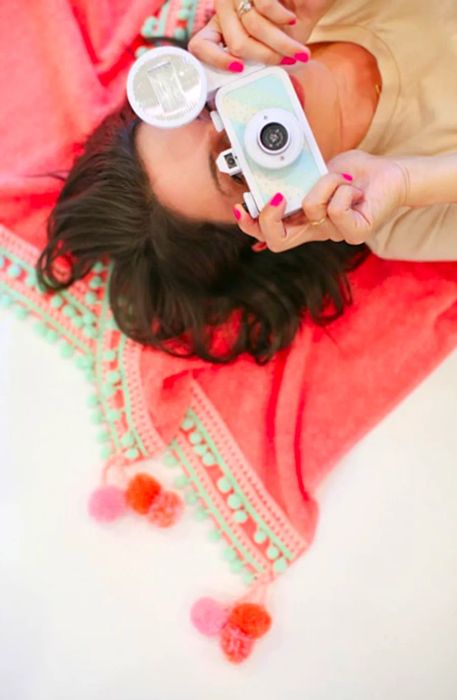 A woman reclining on the towel while holding a camera up to her face