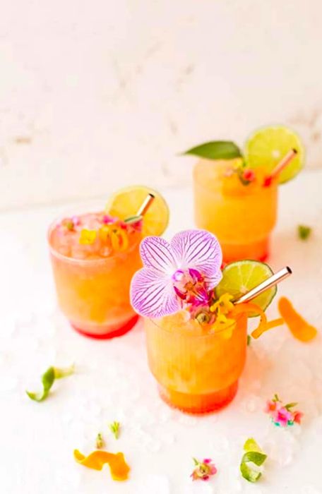 Three pineapple mango rum punch cocktails surrounded by flowers scattered across the table