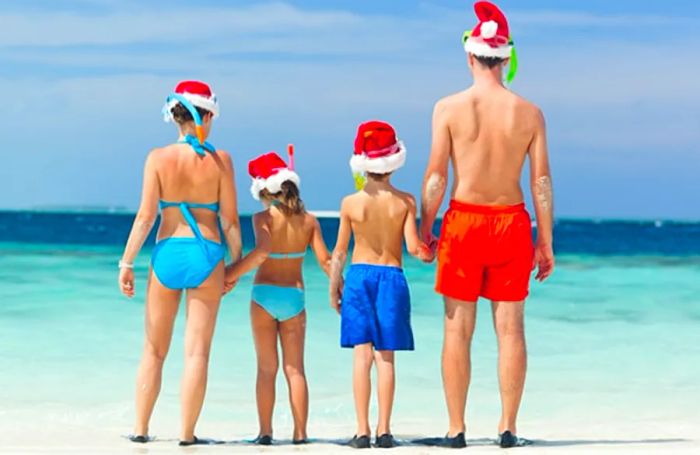 A family standing on a beach in Santa hats, holding hands