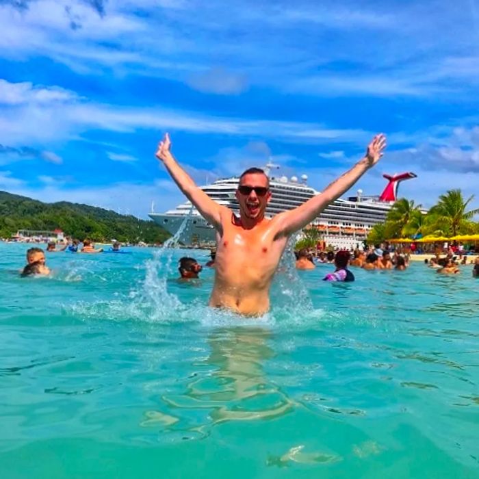 a man at the beach with his arms raised, with a Dinogo ship in the background