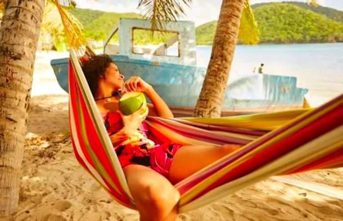 A woman relaxing in a hammock, sipping from a coconut in the Caribbean