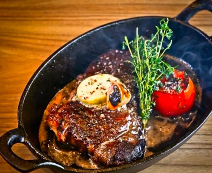 a sizzling plate of steak, garnished with parsley and tomato