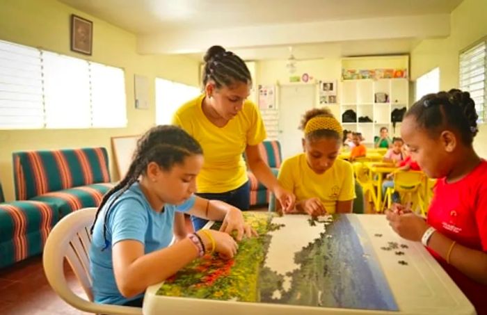 a guest assisting children in solving a puzzle at a children’s improvement center in Amber Cove