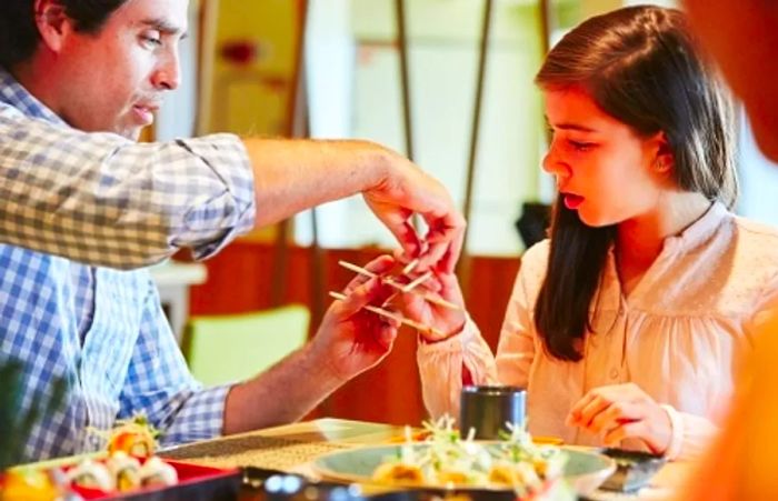 a father instructing his daughter on how to use chopsticks to enjoy sushi