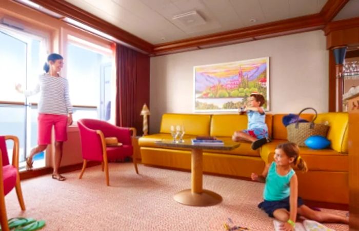 A mother closing the balcony door of her stateroom while her son snaps a photo and her daughter colors in a coloring book.