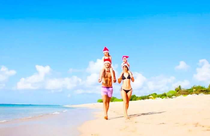 Children perched on their parents’ shoulders, wearing Santa hats while strolling along a beach.