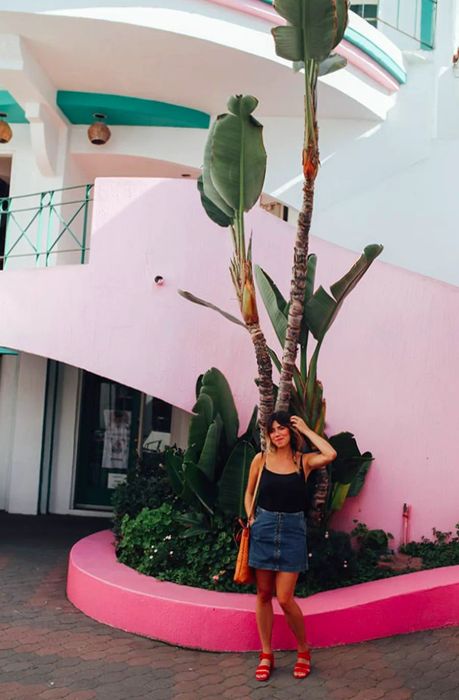 woman taking a photo in front of a pink building adorned with two palm trees