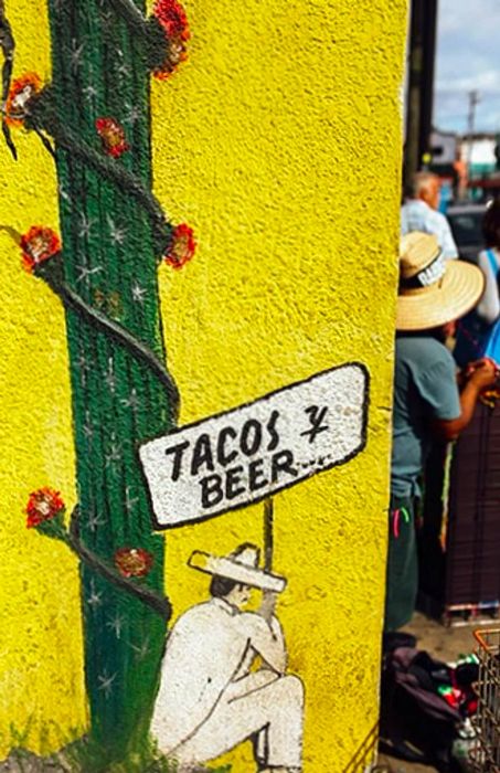 illustration of a man in a sombrero holding a 'tacos y beer' sign while seated next to a cactus