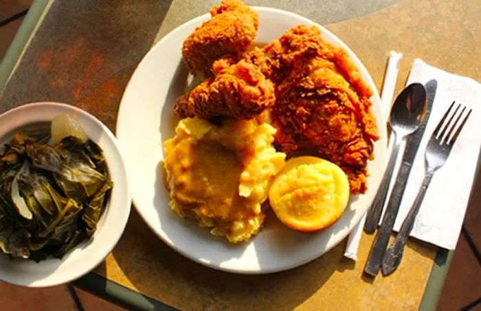 A plate featuring fried chicken, creamy mashed potatoes, cornbread, and a side of collard greens