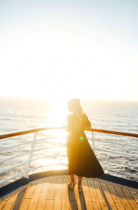 woman striking a pose on the cruise deck as the sun rises in the background