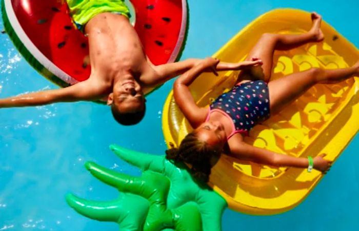 Two children relaxing on inflatable pineapple and watermelon floats while cruising