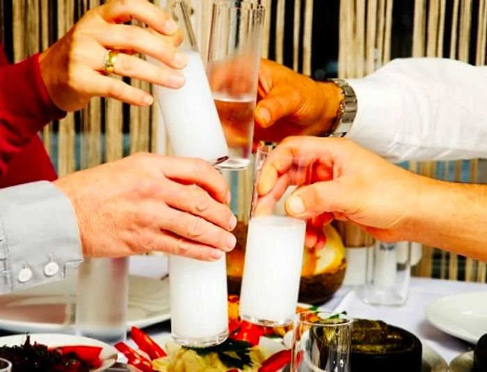 A group of friends toasting with their glasses while enjoying ouzo alongside their meal.