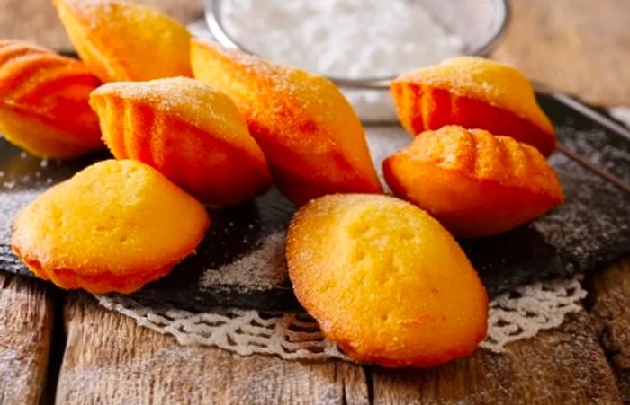 a freshly baked batch of madeleines dusted with powdered sugar, resting on a wooden table