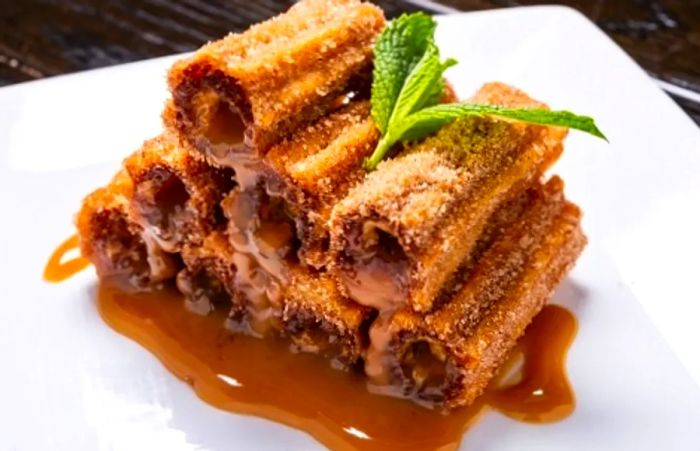 A plate of churros served with cajeta and garnished with a mint leaf