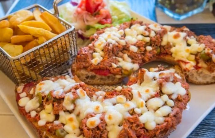 Maltese bread known as hobz biz-zejt, topped with tuna, olives, and cheese, served alongside fries